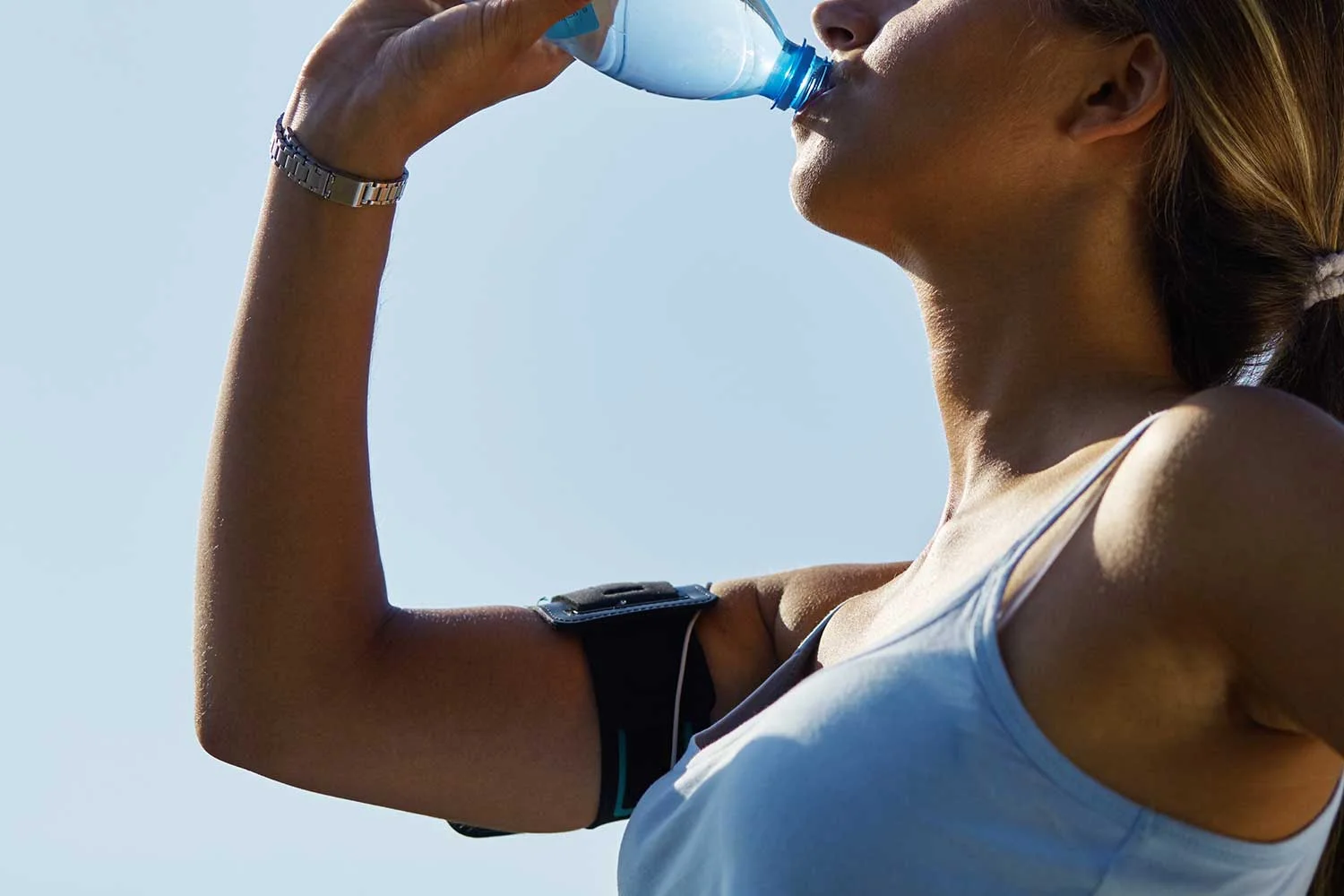 Sporty young woman drinking water from a bottle after training outdoors on a sunny day