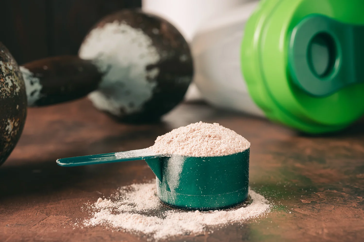 Chocolate meal replacement shake powder in measuring spoon, old rusty dumbbell and shaker on dark background
