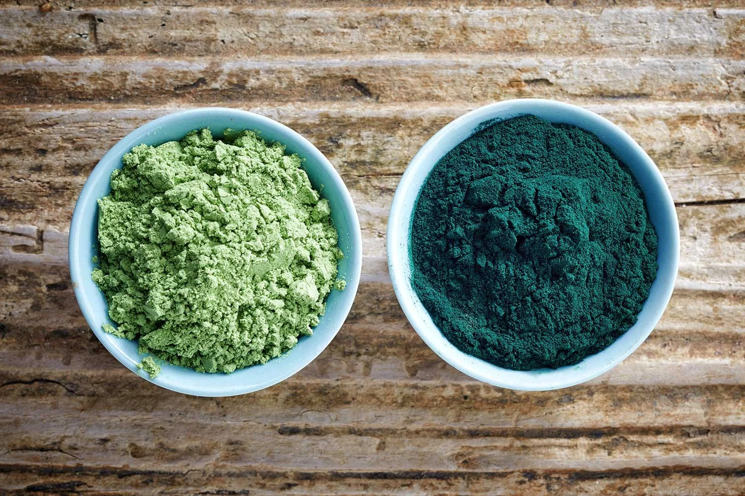 Bowl of organic and non organic superfood powder on wooden background