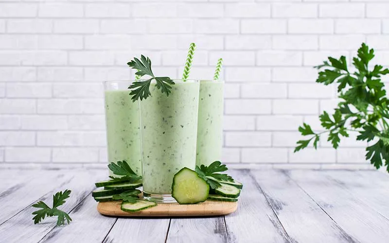 Green smoothie with cucumber and parsley on a wooden background.