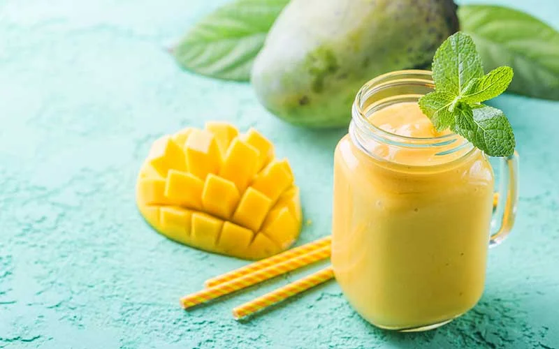 Mango smoothie in a glass jar with fresh mango on a turquoise counter. 