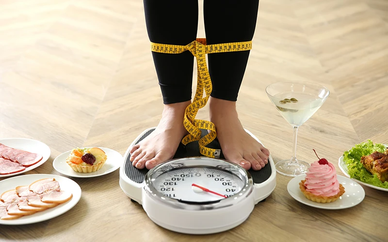 woman with measuring tape standing on scales indoors.
