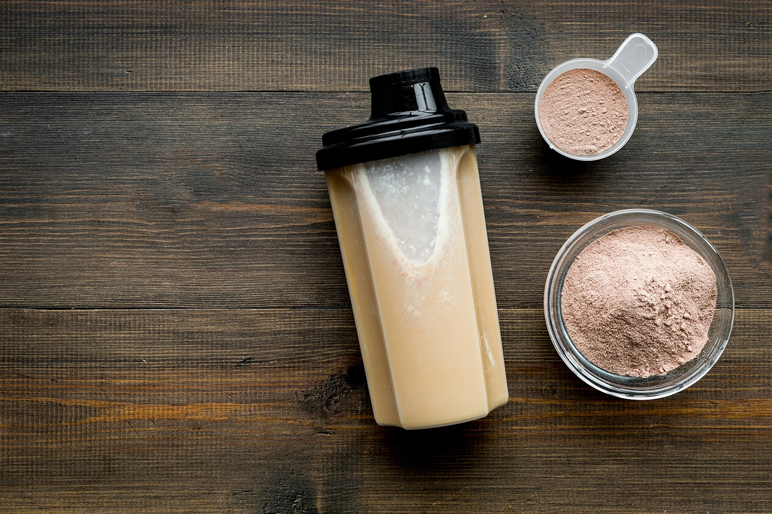 Meal replacement shake powder on scoop and bowl with a shaker on wooden background.