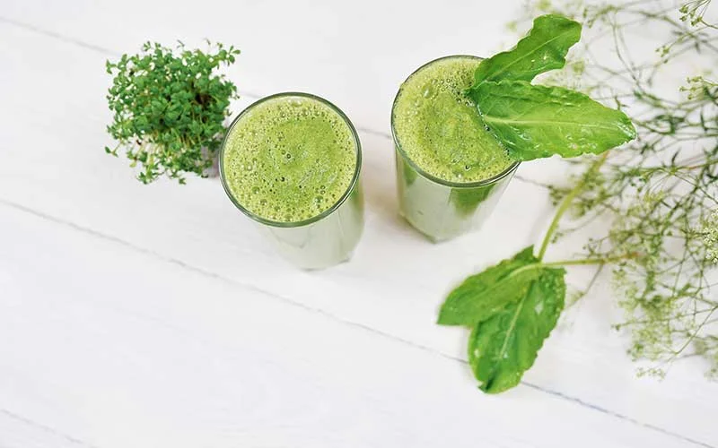 Blended green smoothie with water enhancers on white background.
