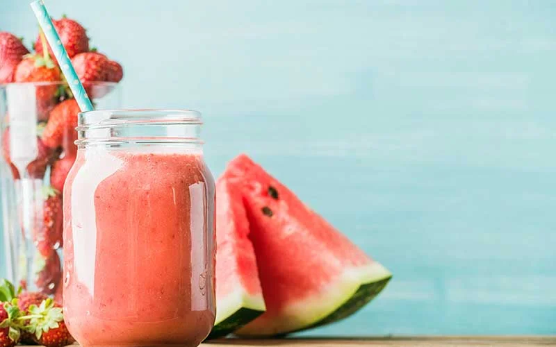Freshly blended watermelon and strawberry fruit smoothie in glass jar with straw.

