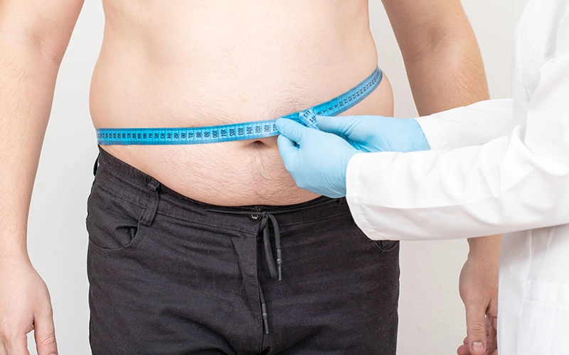 Doctor nutritionist measures bloated belly of a male patient with a measuring tape.
