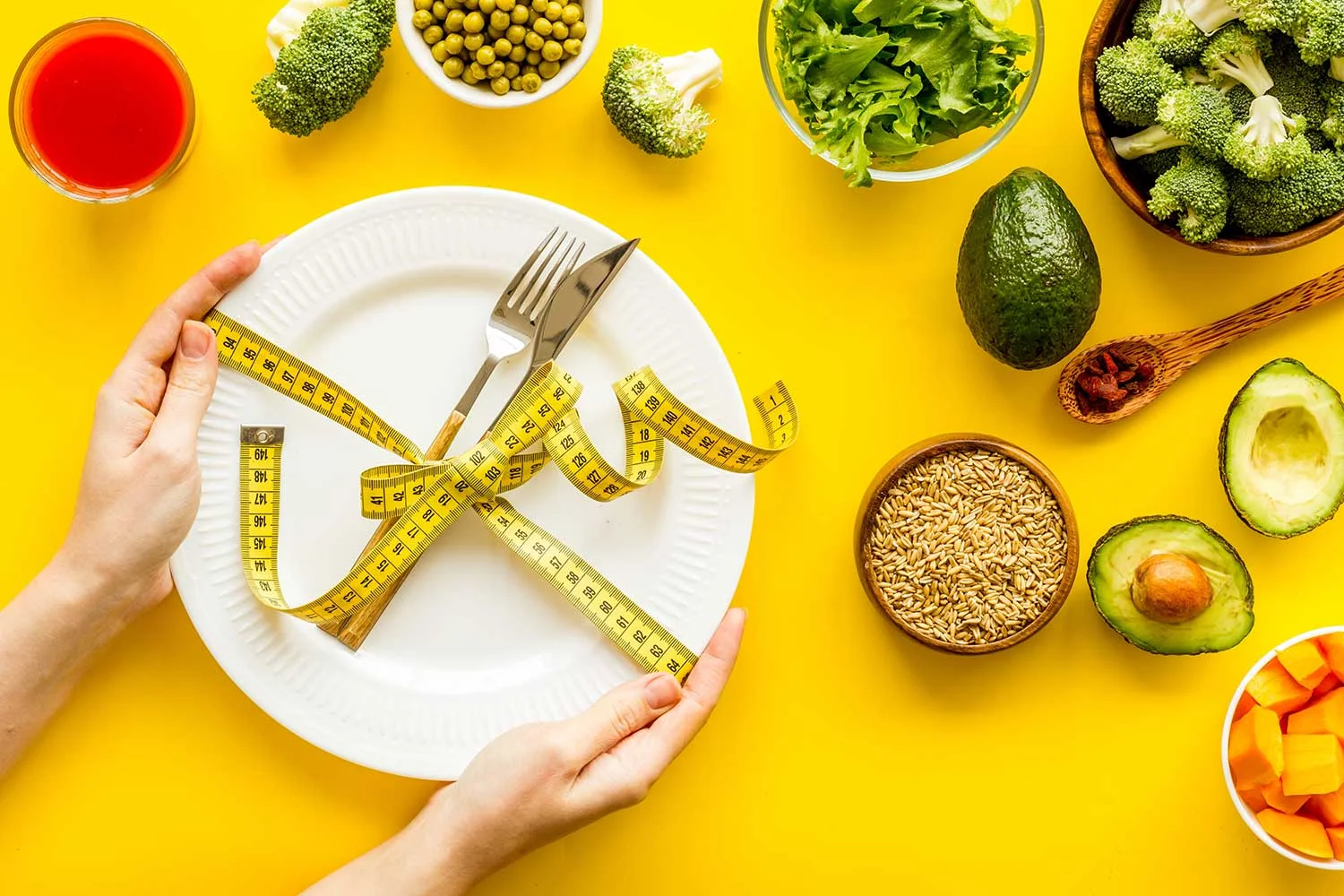 Healthy weight loss recipes.Fork and knife tied with measure tape on plate in hands on yellow background