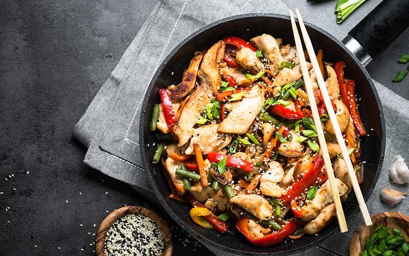 Chicken stir fry with vegetables, soy sauce and sesame seeds in the wok.