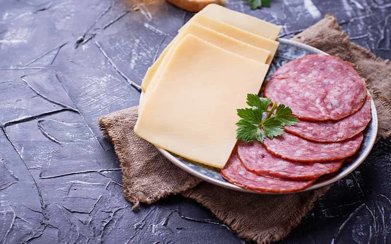 Sliced cheese and salami on plate.
