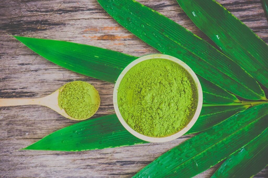 Super green powder in a bowl and scoop on a green leafy wooden background.