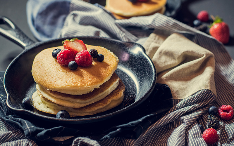 Pancakes with berries in a frying pan on a dark background