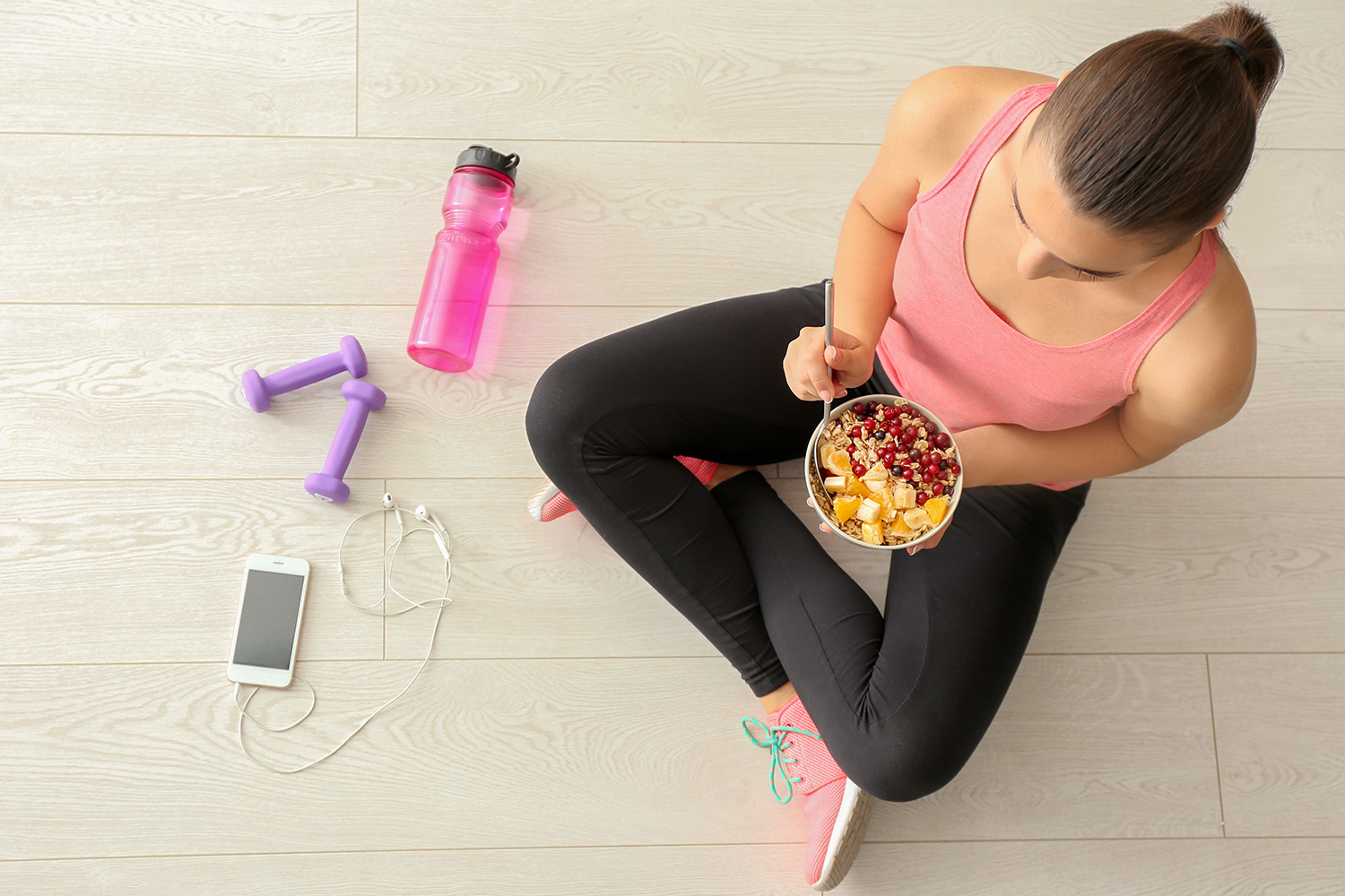 Sporty young woman sitting on the floor with a bowl of healthy food