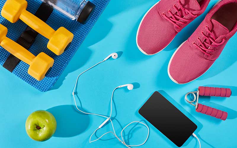 How many carbs should you eat in a day -Top view of sneakers, dumbbells, water bottle, apple and smartphone on blue background