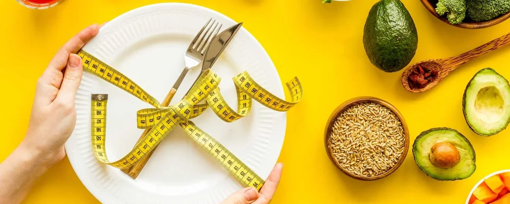 Healthy weight loss recipes.Fork and knife tied with measure tape on plate in hands on yellow background