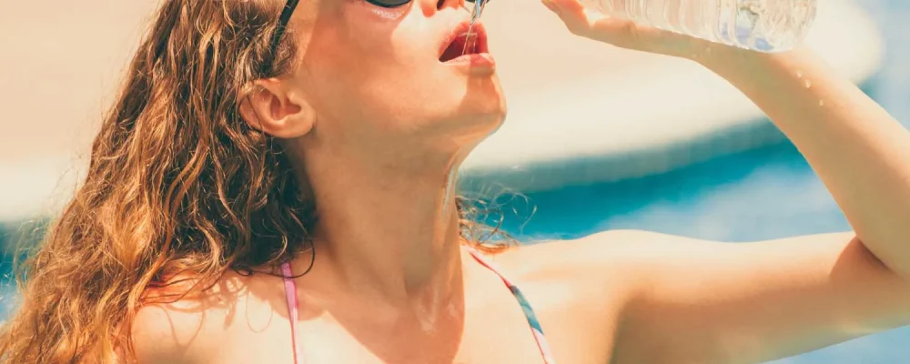 Woman wearing swimsuit drinking water at swimming pool