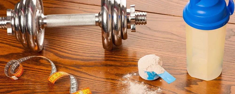 Keto Shake powder in scoop, dumbbell, meter tape and plastic shaker on wooden background.