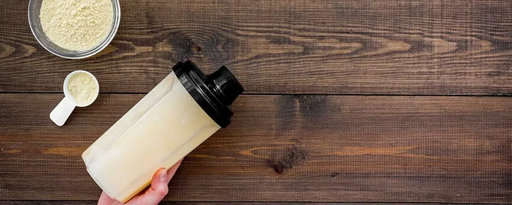 Scoop of meal replacement shake near shaker on dark wooden background