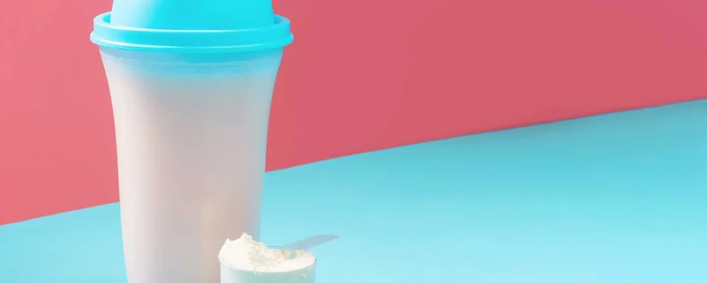Meal Replacement shake and scoop on blue and pink background