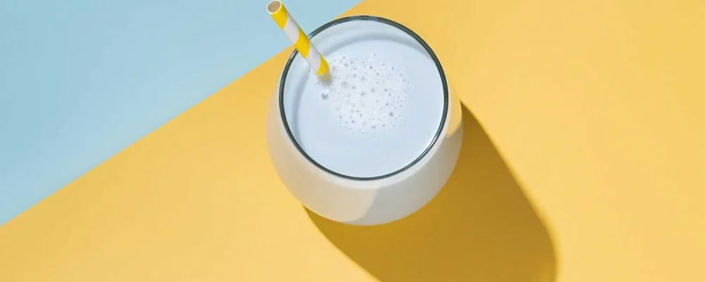 A cup of meal replacement shake with hard shadow on yellow and blue background