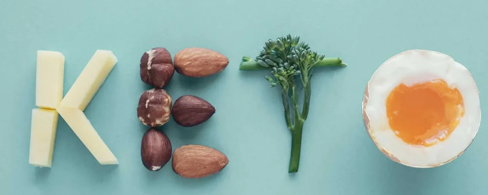 The word “keto” spelled out with keto-friendly, low-carb foods on a pastel blue background
