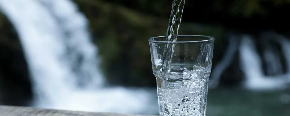 Fresh water pouring into glass on a wooden surface near waterfall