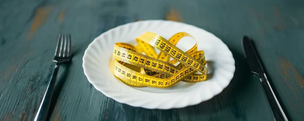 Measuring tape on a plate with fork and knife on wooden background