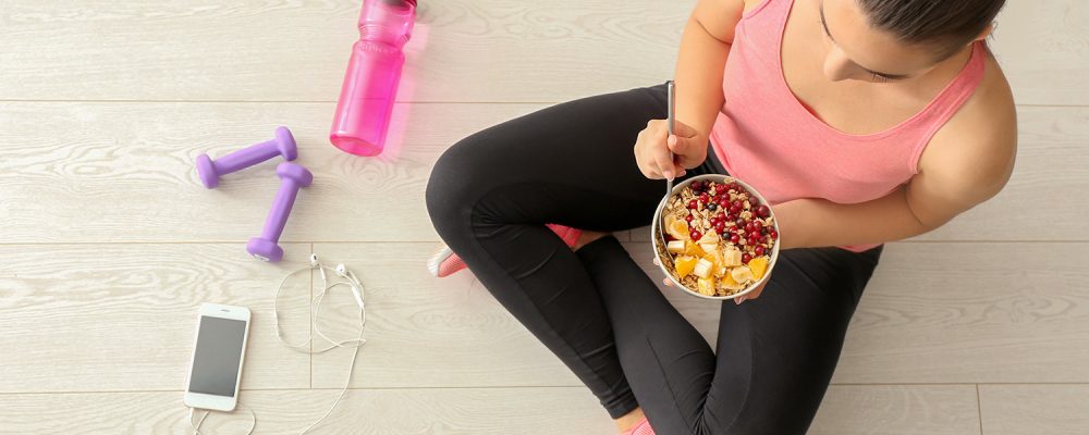 Sporty young woman sitting on the floor with a bowl of healthy food