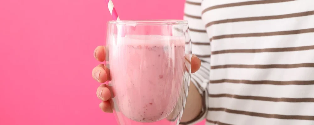 Woman holding glass of homemade tasty milkshake on pink background
